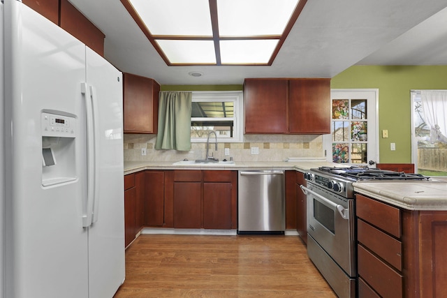 kitchen with a sink, light countertops, appliances with stainless steel finishes, light wood finished floors, and tasteful backsplash