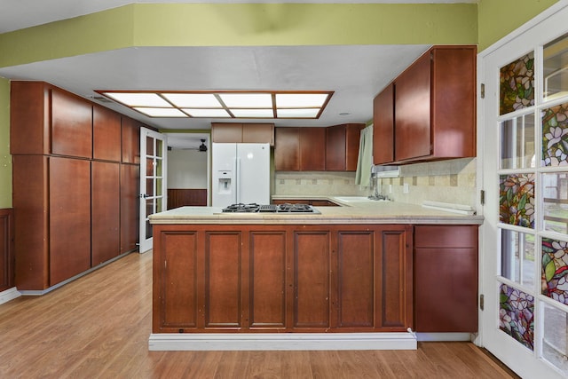 kitchen with white fridge with ice dispenser, light wood finished floors, a peninsula, and a sink