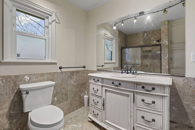 bathroom featuring tile walls, toilet, a stall shower, wainscoting, and vanity