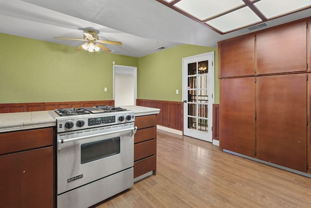 kitchen with light wood finished floors, visible vents, a ceiling fan, a wainscoted wall, and gas stove