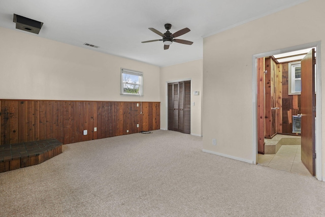 carpeted spare room featuring a wainscoted wall, ceiling fan, visible vents, and wooden walls