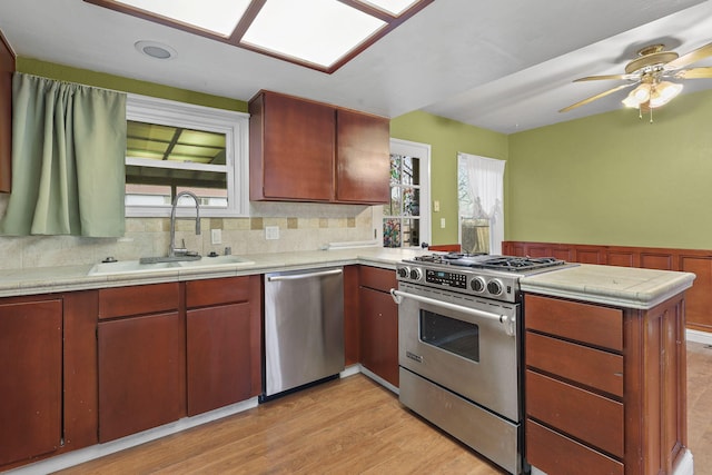 kitchen featuring plenty of natural light, a wainscoted wall, a peninsula, stainless steel appliances, and a sink