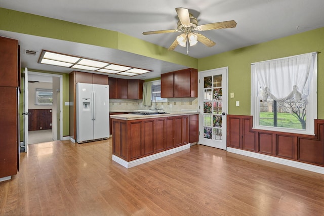 kitchen with a peninsula, light countertops, light wood-type flooring, white fridge with ice dispenser, and tasteful backsplash