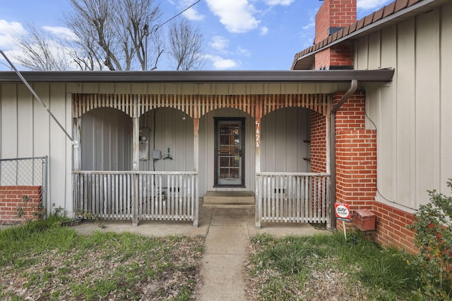 entrance to property with a chimney, a porch, board and batten siding, and brick siding