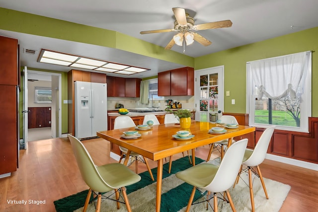 dining space with a wainscoted wall, light wood-style flooring, visible vents, and a ceiling fan