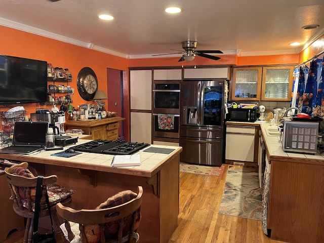 kitchen featuring crown molding, a breakfast bar area, light wood finished floors, tile counters, and black appliances