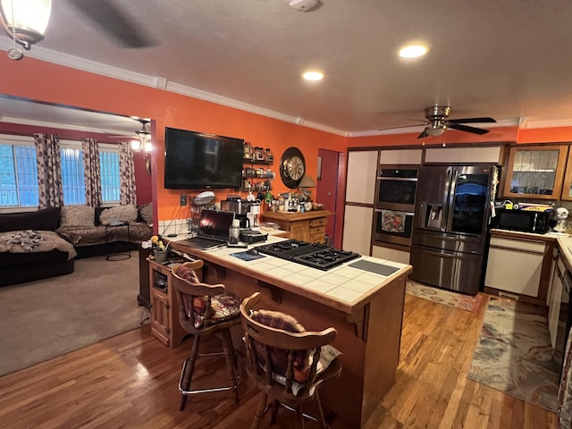 kitchen with ceiling fan, tile counters, black appliances, light wood finished floors, and crown molding