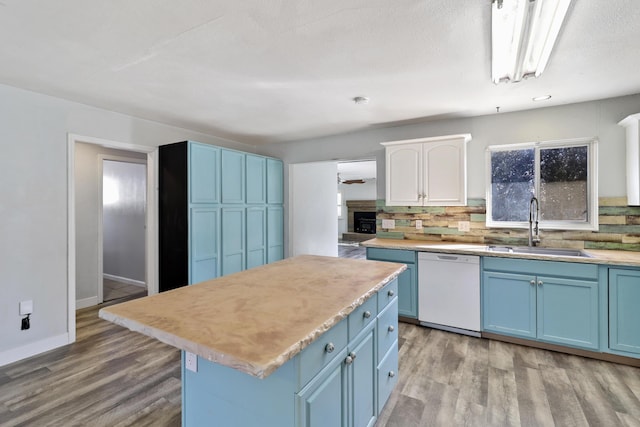 kitchen featuring blue cabinets, a sink, light wood-style floors, dishwasher, and tasteful backsplash