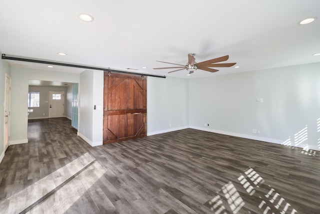 empty room with dark wood-type flooring, recessed lighting, baseboards, and a barn door