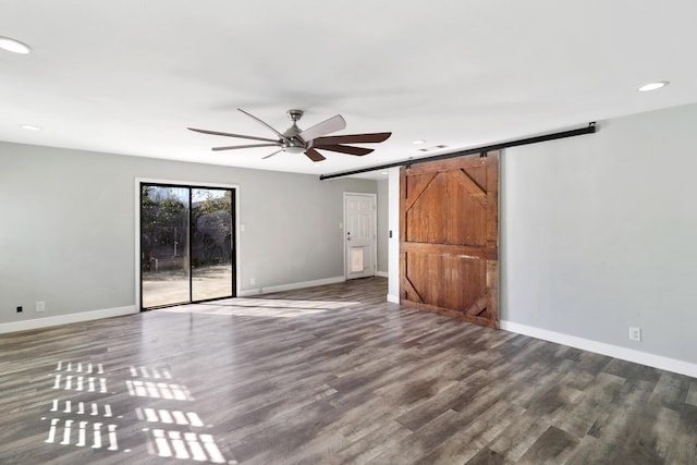 interior space with ceiling fan, a barn door, wood finished floors, and baseboards