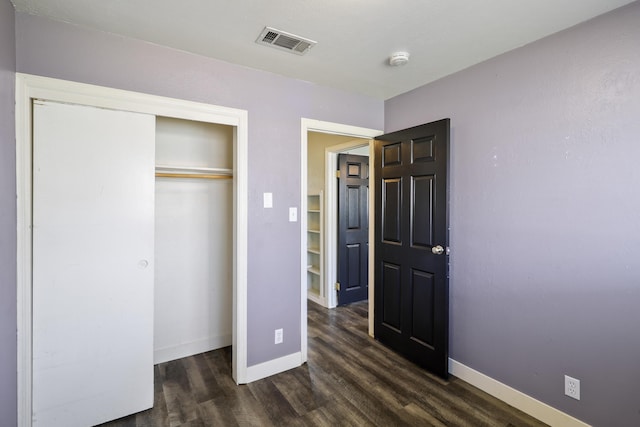 unfurnished bedroom with baseboards, visible vents, dark wood finished floors, and a closet