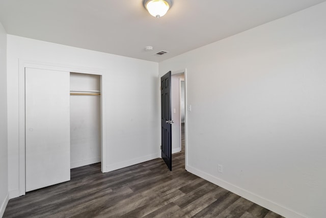 unfurnished bedroom with dark wood-style flooring, a closet, visible vents, and baseboards