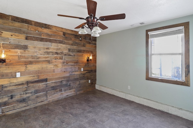 spare room with visible vents, concrete floors, wooden walls, and baseboards