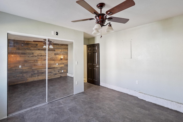 unfurnished bedroom with finished concrete flooring, wood walls, a ceiling fan, and baseboards