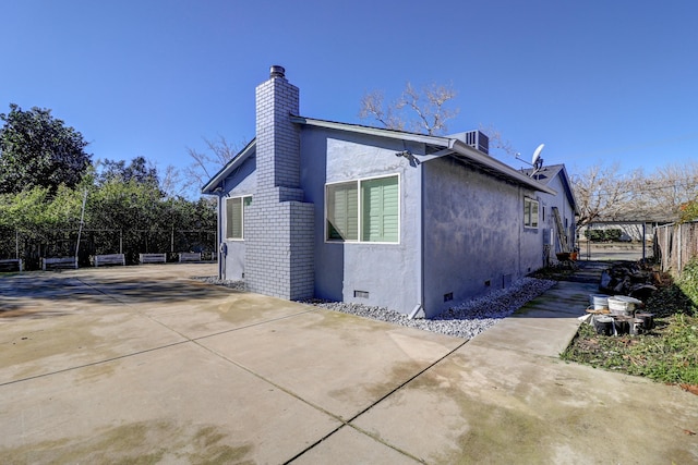 view of property exterior featuring central air condition unit, fence, crawl space, stucco siding, and a chimney