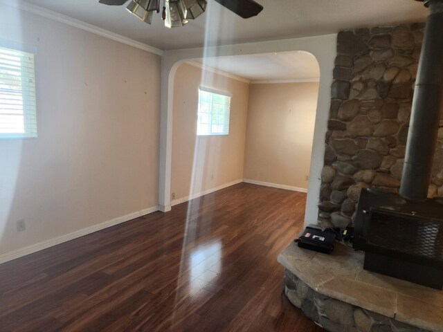 unfurnished living room featuring a wood stove, arched walkways, a ceiling fan, and ornamental molding