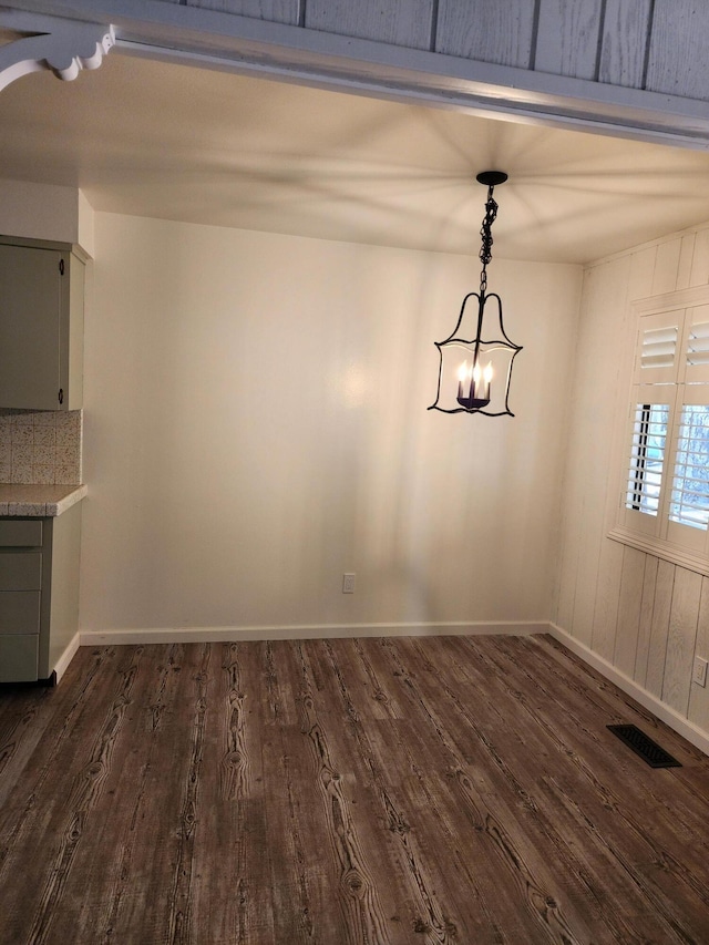 unfurnished dining area featuring baseboards, a notable chandelier, visible vents, and dark wood-type flooring