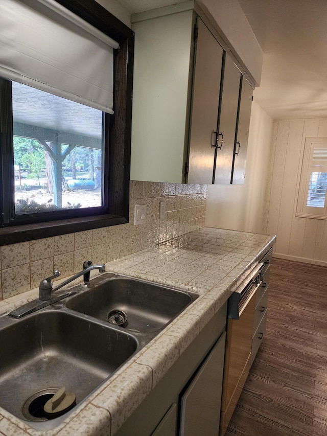 kitchen featuring tasteful backsplash, tile countertops, dark wood-style floors, dishwashing machine, and a sink