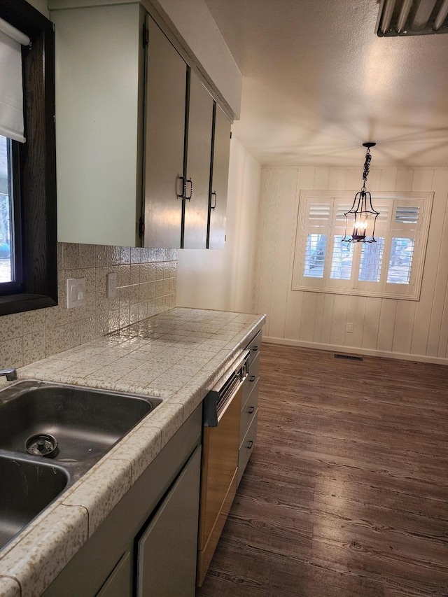 kitchen featuring tasteful backsplash, dishwasher, dark wood-style flooring, hanging light fixtures, and a sink