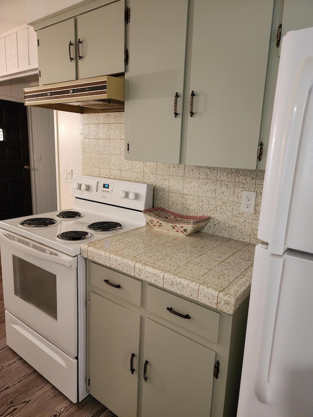 kitchen with white appliances, decorative backsplash, tile countertops, dark wood-type flooring, and under cabinet range hood