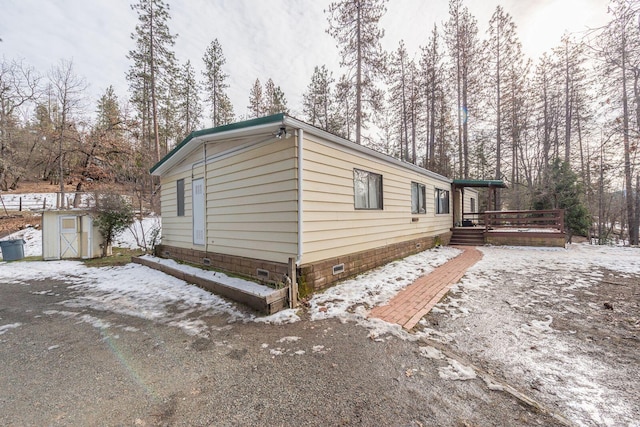 view of snow covered exterior featuring crawl space, an outbuilding, a storage shed, and a wooden deck