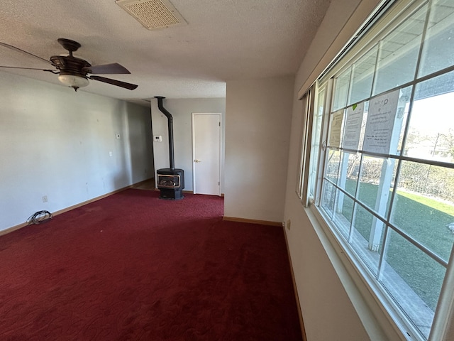 unfurnished living room featuring carpet floors, visible vents, a wood stove, a textured ceiling, and baseboards