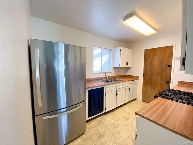 kitchen featuring white dishwasher, butcher block counters, a sink, white cabinets, and freestanding refrigerator