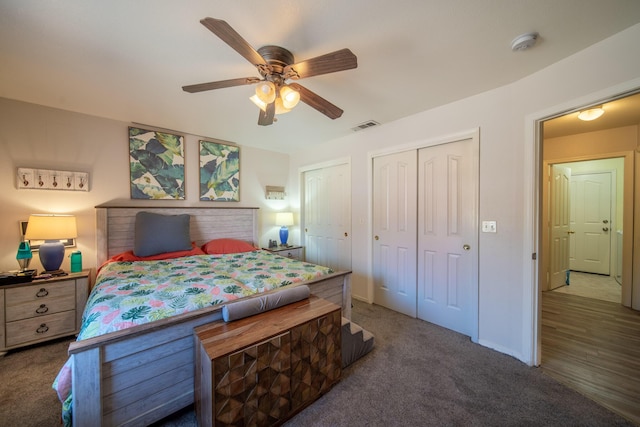 carpeted bedroom with baseboards, visible vents, two closets, and a ceiling fan