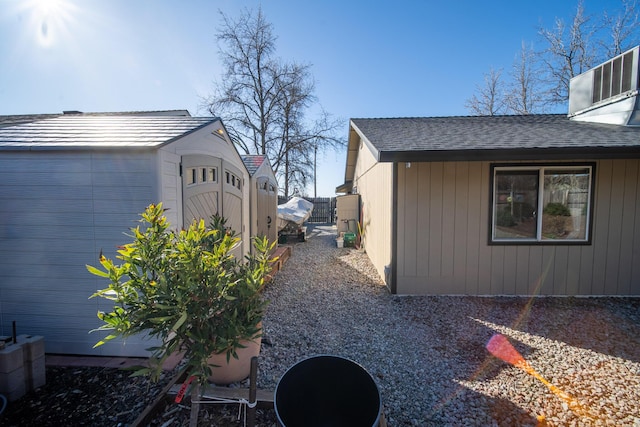 view of side of property featuring a shingled roof, an outdoor structure, and fence