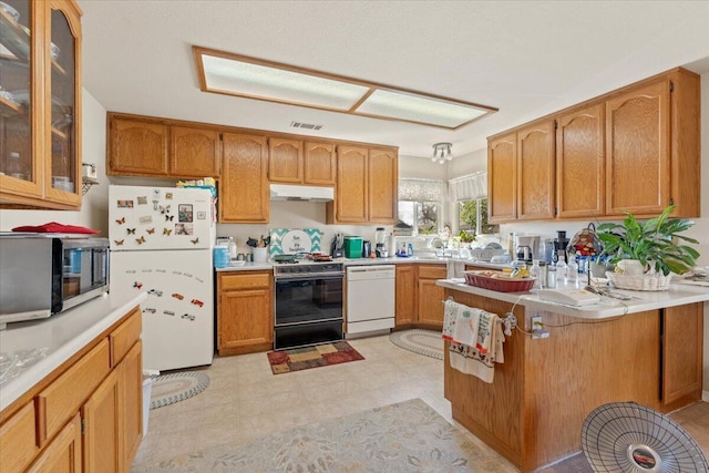 kitchen with light countertops, glass insert cabinets, a peninsula, white appliances, and under cabinet range hood