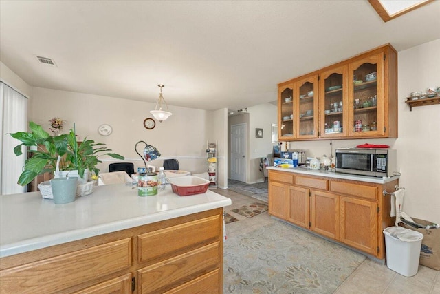 kitchen featuring visible vents, brown cabinetry, glass insert cabinets, stainless steel microwave, and light countertops