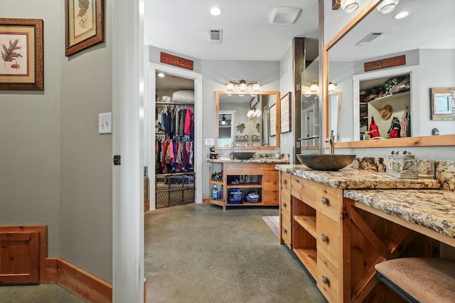 bathroom with concrete flooring, a textured wall, visible vents, vanity, and a walk in closet