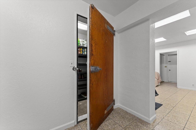 hallway with light floors, a textured wall, and baseboards