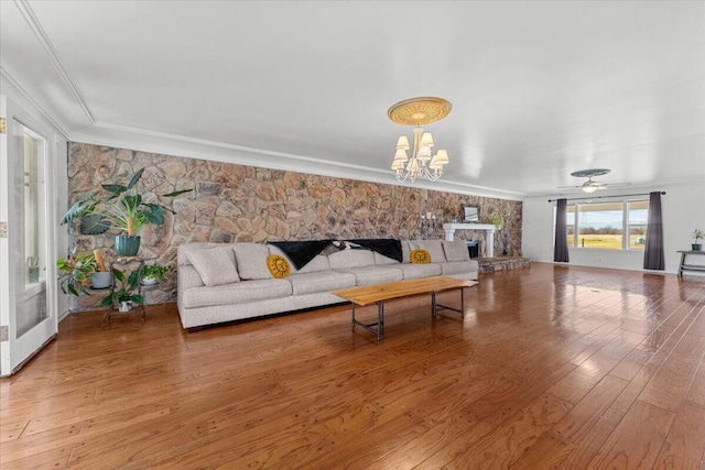 living room with ornamental molding, a stone fireplace, ceiling fan with notable chandelier, and wood finished floors