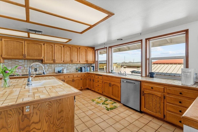 kitchen featuring tile countertops, stainless steel dishwasher, backsplash, and a sink