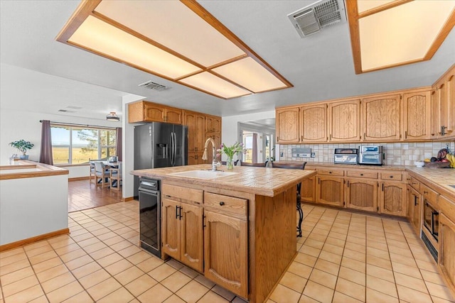 kitchen with tasteful backsplash, black fridge, a sink, and visible vents