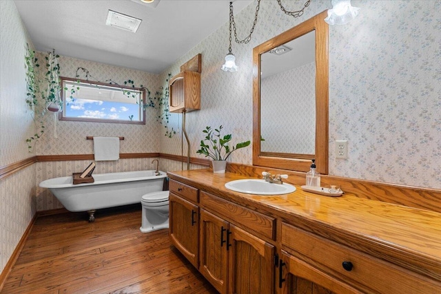 full bath featuring wallpapered walls, hardwood / wood-style floors, a wainscoted wall, and a soaking tub