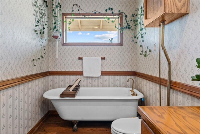 full bath with toilet, wallpapered walls, a freestanding bath, and wainscoting