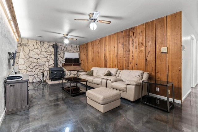 living room featuring finished concrete flooring, visible vents, a wood stove, ceiling fan, and wooden walls