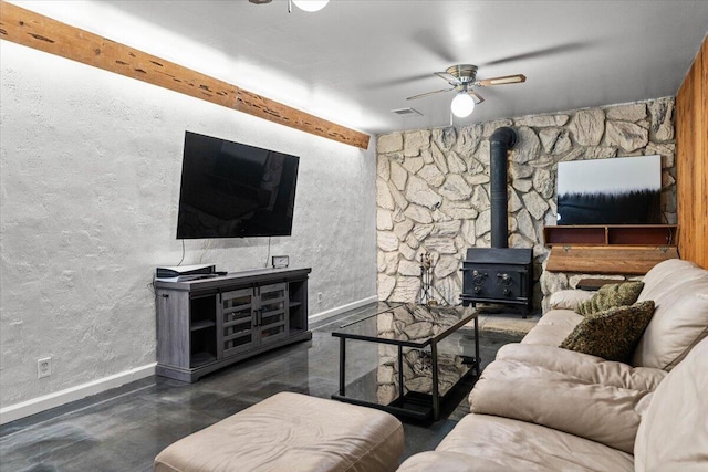 living area with visible vents, a wood stove, ceiling fan, concrete flooring, and baseboards