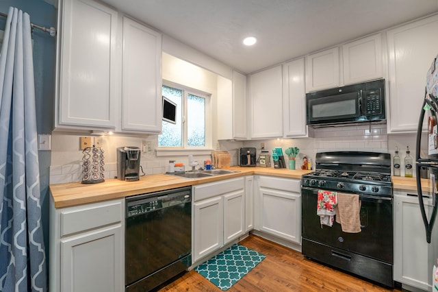 kitchen with butcher block counters, white cabinets, backsplash, and black appliances