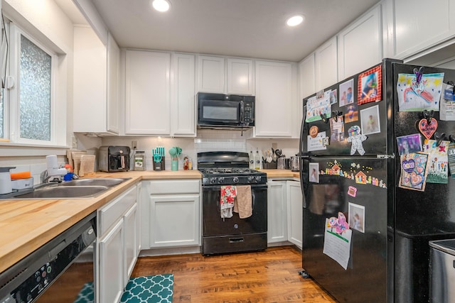 kitchen featuring black appliances, wood finished floors, a sink, and white cabinets