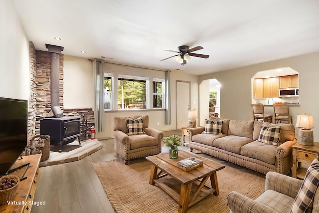 living area featuring arched walkways, ceiling fan, light wood-style flooring, recessed lighting, and a wood stove