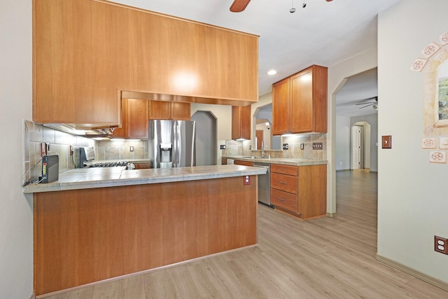 kitchen featuring arched walkways, ceiling fan, a peninsula, stainless steel appliances, and light countertops