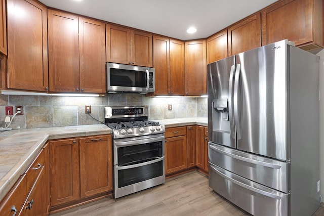 kitchen featuring stainless steel appliances, light wood-type flooring, brown cabinetry, and decorative backsplash