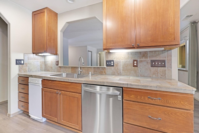 kitchen with a sink, light countertops, light wood-type flooring, dishwasher, and tasteful backsplash