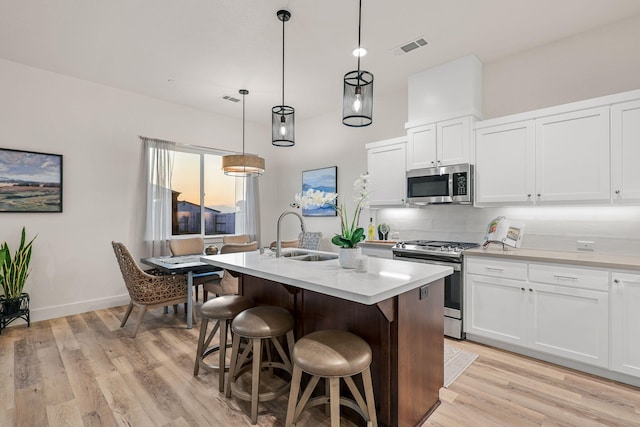 kitchen featuring a kitchen island with sink, stainless steel appliances, a sink, visible vents, and light countertops