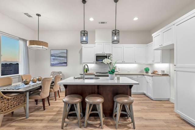 kitchen with light wood finished floors, visible vents, stainless steel microwave, and a sink