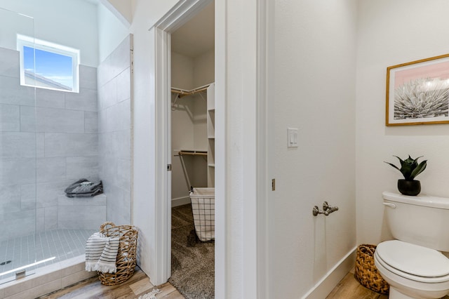 full bath with wood finished floors, a tile shower, toilet, and a walk in closet