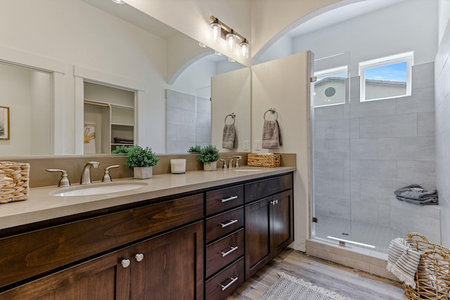 bathroom featuring wood finished floors, double vanity, tiled shower, and a sink